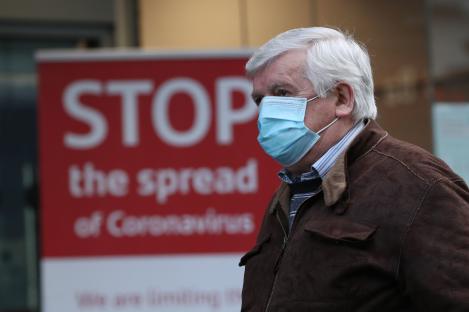 Man wearing a face mask walks past a sign that says