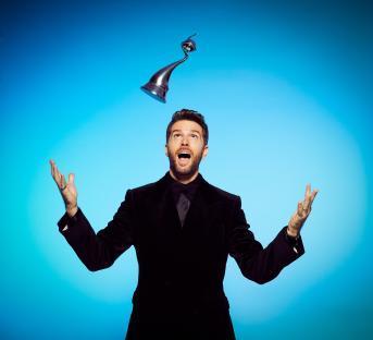 Joel Dommett, host of the National Television Awards, looking up at a trophy.