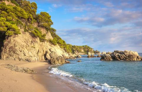 Sandy beach with rocky cliffs and clear blue water.