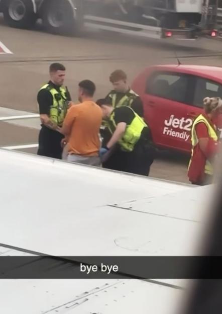 A man being arrested by police officers on an airplane wing.