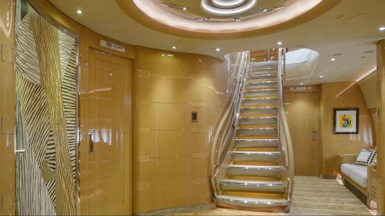 Interior of a luxurious private jet, showing a staircase and gold-toned walls.