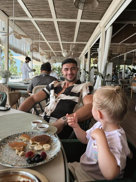 Tommy Fury and a toddler eating pancakes at an outdoor restaurant.
