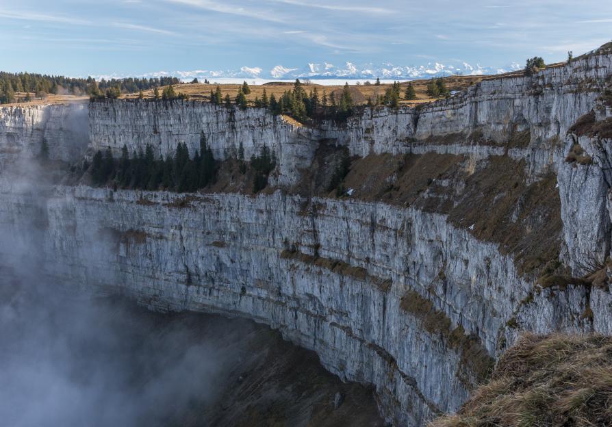 Creux du Van natural amphitheatre in the Jura mountains, Switzerland, with snowy Alps in the background.
