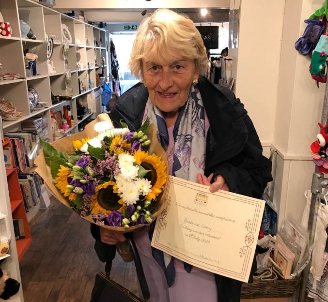 Beatrice Corry holding a bouquet of flowers and a certificate recognizing her as a "star volunteer."