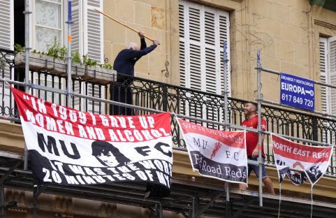 A man on a balcony threatens a Manchester United fan with a stick.