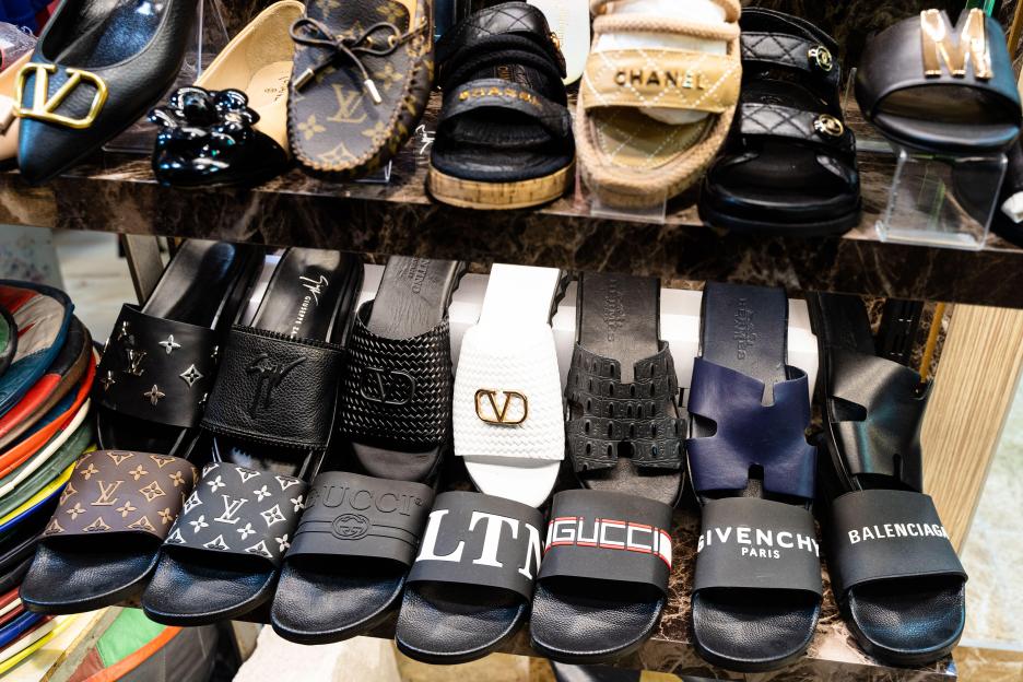 Close-up of a shelf with various fake fashion brand shoes and sandals.