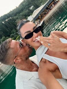 A woman showing off her engagement ring while being kissed by a man.
