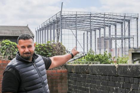 Man pointing at a large metal warehouse under construction.