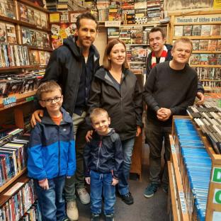 Photo of Ryan Reynolds and Rob McElhenny with a family in a DVD store.
