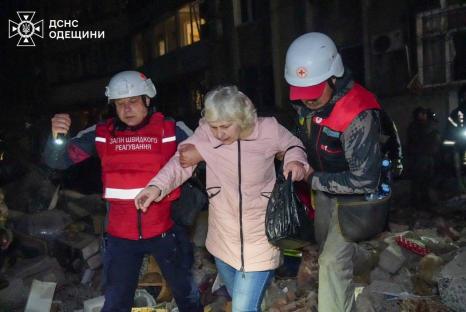 Emergency personnel evacuating a woman from a damaged building.