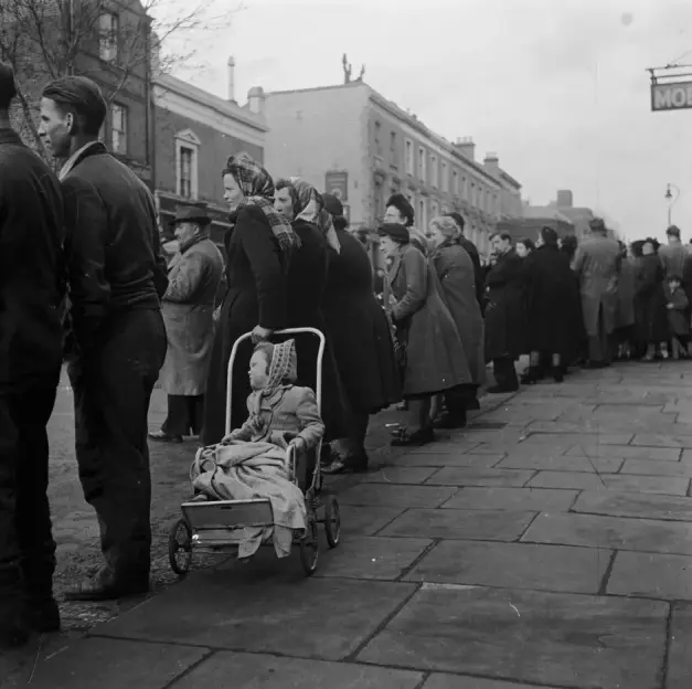 A long queue of people, including a child in a pram.