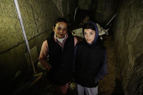 Two women standing in a dark, damaged basement.