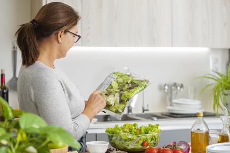 Woman examining the nutrition label on a bag of salad in her kitchen.