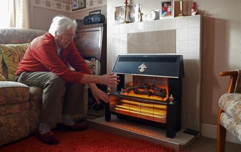 Elderly woman warming herself by an electric fire.