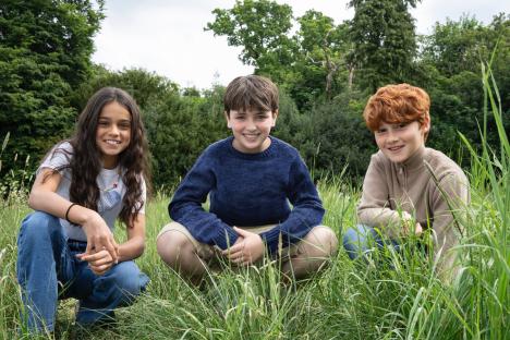 Three smiling children crouching in tall grass.