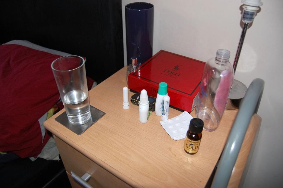 A bedside table with a glass of water, bottles of "poppers", a red Polo box, and baby oil.