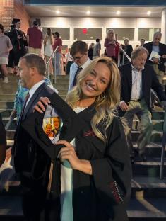 Graduate in cap and gown holding a photo of two women.