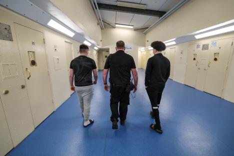 Prison officer escorting two teenage inmates down a prison corridor.