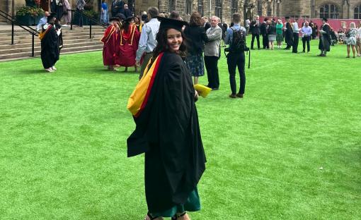 Graduate in cap and gown on a lawn with other graduates and guests.