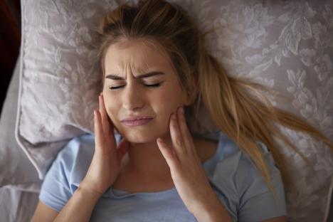 Woman in bed holding her jaw, experiencing bruxism.