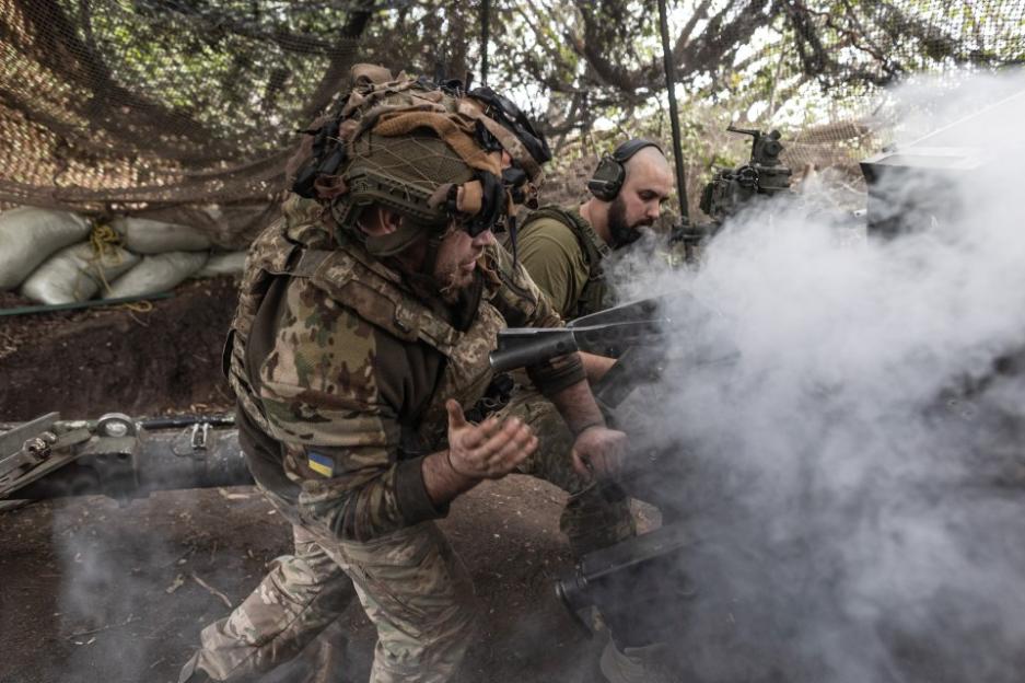 Two soldiers fire an artillery weapon, emitting a cloud of white smoke.