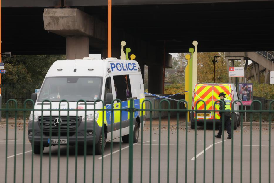 Two police vans are parked under an overpass at Bescot Stadium railway station, with a police officer walking near one van.