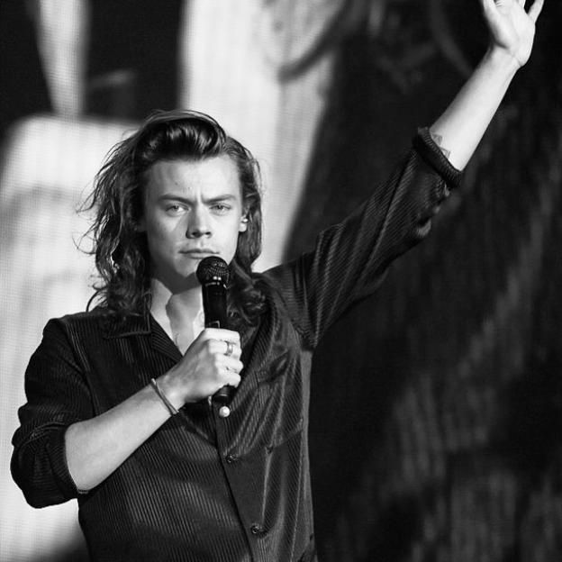 Black and white photo of Harry Styles holding a microphone and waving.