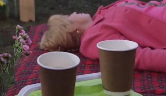 Woman lying on a blanket with two coffee cups nearby.