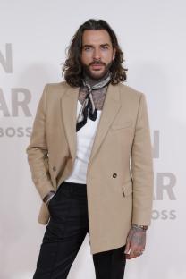 a man with long hair and a scarf around his neck stands in front of a wall that says boss