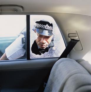 Police officer examining the interior of a car with a broken rear window.