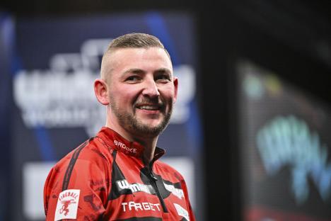 Nathan Aspinall smiling after winning a darts match.