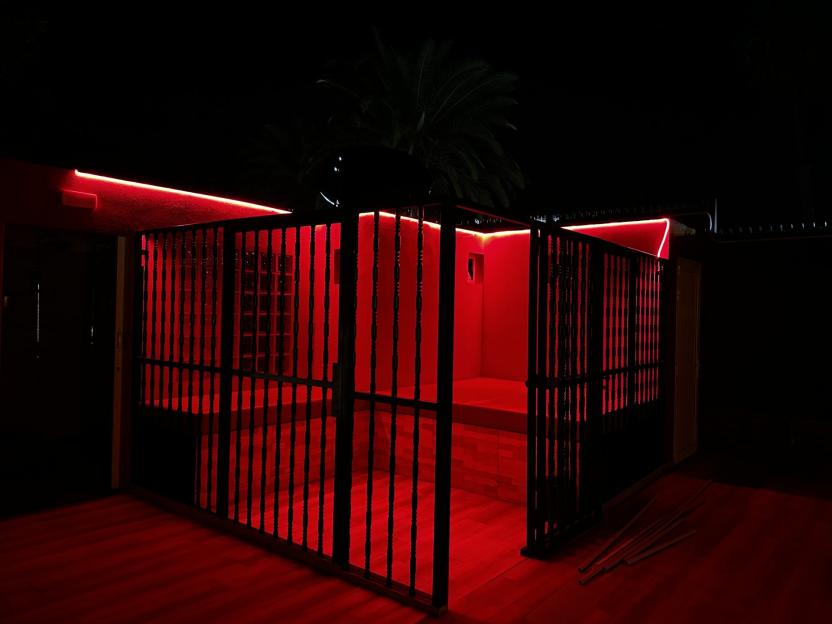 Red-lit outdoor enclosure with a black metal gate.