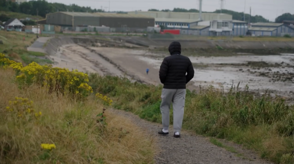 Person walking away from the camera on a path near the coast.