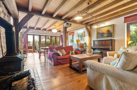 Interior view of a large living room with exposed wooden beams, a wood-burning stove, and comfortable sofas.