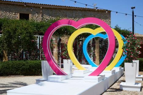 Interlocking heart-shaped arches in pink, yellow, and blue, set on a white platform.