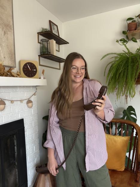 Kassadi Gabriel holding a dark brown landline phone with a coiled cord, smiling at the camera.