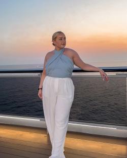 a woman in a blue top and white pants stands on a balcony overlooking the ocean