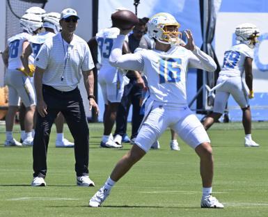Los Angeles Chargers quarterback Jameson Wang #16 throws a football during practice, with head coach Jim Harbaugh watching.