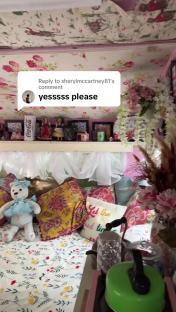 Interior of a caravan with a floral theme, including a bed with pillows and a shelf with decorative items.