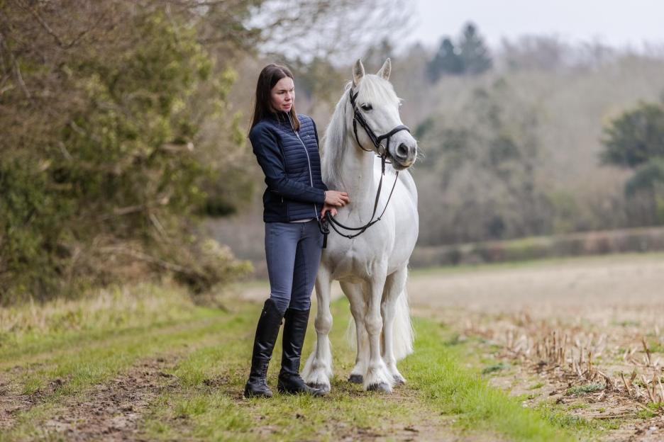 Woman standing with a white horse in a field.