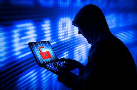 Silhouette of a hooded figure using a laptop with an unlocked padlock on the screen.