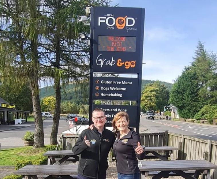 Rich James Cross and Sarah standing in front of The Real Food Cafe in Tyndrum.