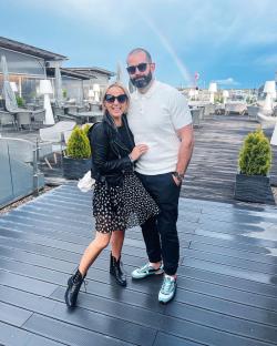 Couple posing on a rooftop terrace with a rainbow in the background.