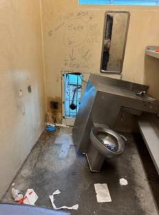 Damaged jail cell with graffiti and a broken sink.