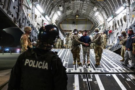 U.S. military personnel escorting deported gang members off a plane.