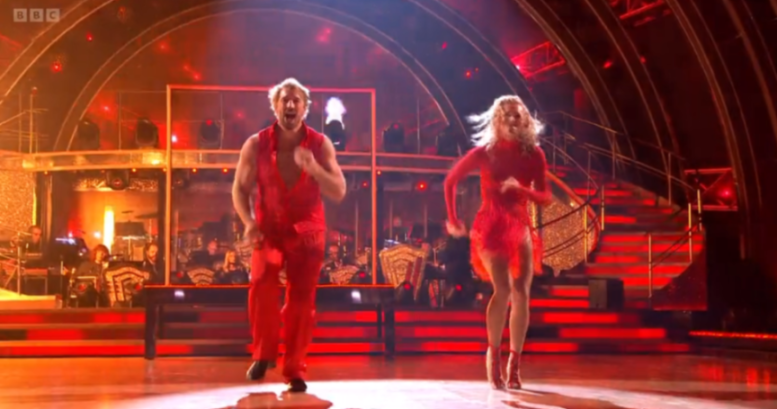 Two dancers in red outfits perform on a brightly lit stage.