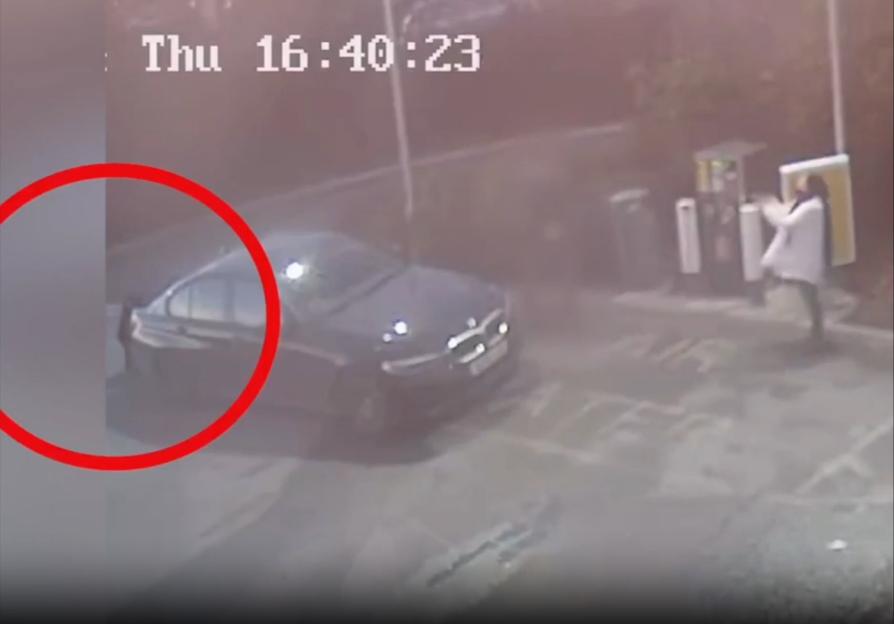 Surveillance footage showing a person dressed in a white coat at a gas station with a black car.