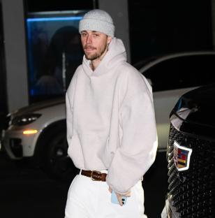 Justin Bieber wearing a light-colored hoodie, knit hat, and white pants.