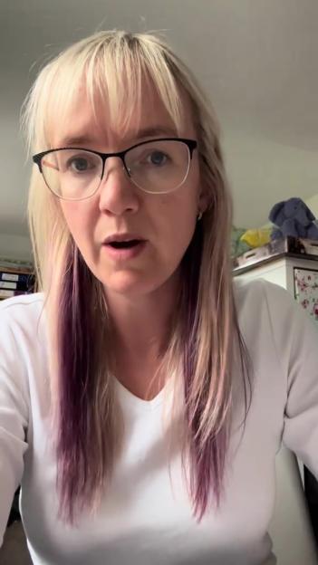 Woman with glasses and purple streaks in her blonde hair speaks to the camera.