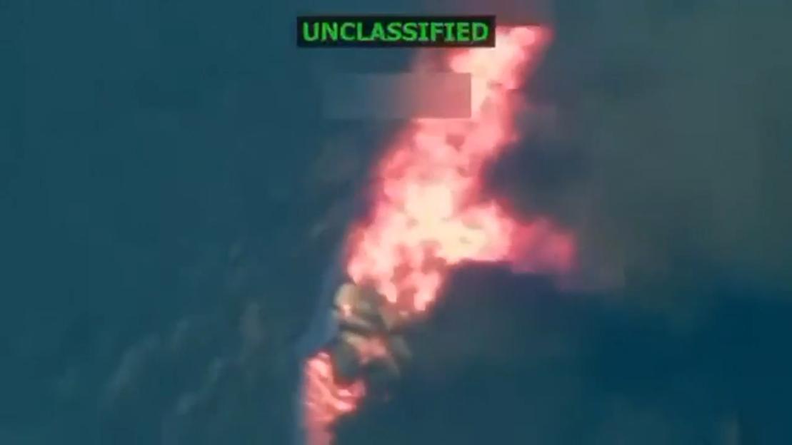 An "UNCLASSIFIED" video showing a vessel on fire and emitting smoke on a dark body of water.